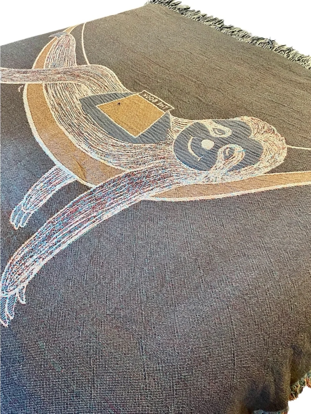 Outcasty cotton throw, relaxing sloth with book, shown on a Queen size bed